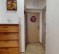 Folyosó egy 3 szobás lakásban komóddal, fa dekor padlóval és díszes dekorációval az ajtókon.