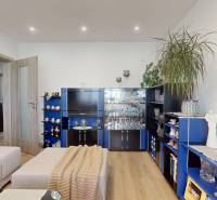 Nappali kanapéval, kék nappali szekrénysorral és fa mintázatú padlóval egy háromszobás lakásban.