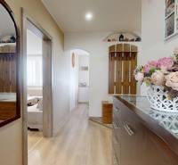 3 szobás lakás folyosója tükörrel, fa részletekkel és dekoratív virággal a komódon.