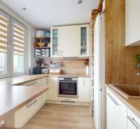 Konyha fa mintázatú padlóval, világos szekrényekkel és kilátással egy háromszobás lakásban.