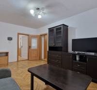 Nappali sötét bútorokkal és fa dekorációjú padlóval egy kétszobás lakásban.