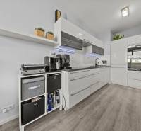 Konyha egy kétszobás lakásban fehér szekrényekkel és fa mintázatú padlóval.