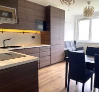 Konyha egy háromszobás lakásban sötét bútorokkal és fa dekoros padlóval.