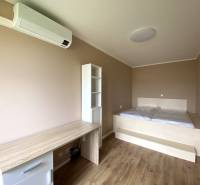 Hálószoba egy háromszobás lakásban fa dekor padlóval, ággyal és íróasztallal.