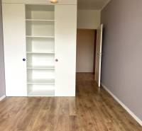 Szoba fehér polccal és fa dekorációjú padlóval egy háromszobás lakásban.