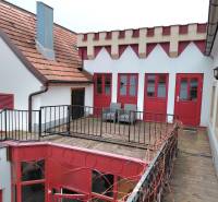 Udvar terasszal és piros ajtókkal, amelyet az eisenstadti Hauptstraße irodáinak építészete vesz körül.