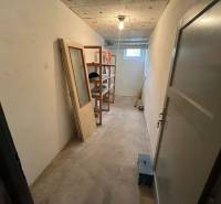 Tároló polcokkal és ablakkal egy háromszobás lakásban, padlóburkolat nélkül.