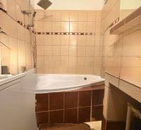 Fürdőszoba egy kétszobás lakásban sarokkáddal és bézs csempékkel.