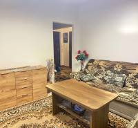 Nappali egy kétszobás lakásban fa komóddal és mintás szőnyeggel.