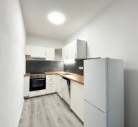 Konyha egy egyszobás lakásban fekete csempével és fa mintázatú padlóval.