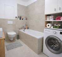 Egy szobás lakás fürdőszobája káddal, mosógéppel és WC-vel, kiegészítve tárolóhellyel.