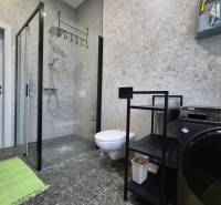 Fürdőszoba egy egyszobás lakásban zuhanyzóval, mosógéppel és tároló polccal.