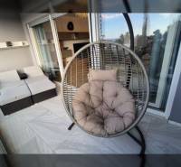 Pihenőterasz rekreációs apartmanhoz kerek hintaszékkel és rattan ülőgarnitúrával.