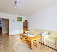 Nappali fa mintás padlóval, krémszínű kanapéval és fa bútorokkal egy háromszobás lakásban.