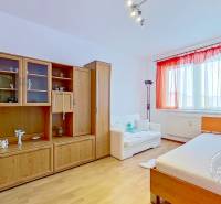 Szoba egy háromszobás lakásban fa dekor bútorokkal és ablakkal szemben lévő ággyal.