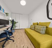 Szoba egy négy szobás lakásban zöld kanapéval, számítógéppel és fa dekor padlóval.