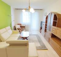 Nappali egy kétszobás lakásban krémszínű kanapéval, zöld fallal és bútorszettel.