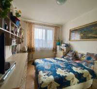 Hálószoba ággyal, polcokkal és fapadlóval egy háromszobás lakásban.