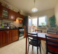 Konyha egy háromszobás lakásban fa szekrényekkel, étkezőasztallal és erkéllyel rendelkező ablakkal.