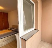 Hálószoba egy kétszobás lakásban ággyal, fa dekorációjú padlóval és teraszra nyíló hozzáféréssel.