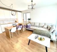 Nappali konyhával egy háromszobás lakásban, világos kanapé, fa dekoros padló.