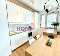 Konyha egy háromszobás lakásban fehér szekrényekkel és fa dekorációjú padlóval.