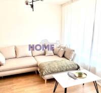 Nappali egy háromszobás lakásban kanapéval, asztallal és fa mintázatú padlóval.