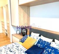 Hálószoba egy háromszobás lakásban ággyal, színes párnákkal és tárolóhelyekkel.