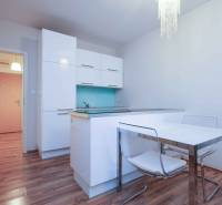 Konyha egy kétszobás lakásban fehér szekrényekkel és fa mintázatú padlóval.