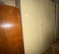 Szekrény a családi házban, mellette barna bútor és geometrikus mintás szőnyeg.