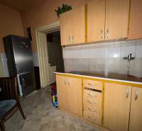 Családi ház konyhája hűtőszekrénnyel, szekrényekkel és csempézett padlóval.