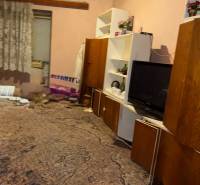 Szoba családi házban szőnyeggel, polcokkal, televízióval és függönyökkel.