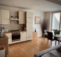 Konyha egy kétszobás lakásban étkezőasztallal és fa mintázatú padlóval.