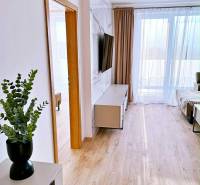 3 szobás lakás belső tere fa dekor padlóval, TV-vel és függönyökkel.