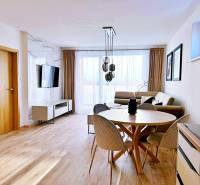 Nappali egy háromszobás lakásban világos bútorokkal és fa dekorációjú padlóval.