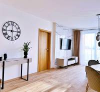 Nappali egy háromszobás lakásban, fa dekoros padlóval, asztallal és televízióval.