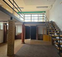 Kereskedelmi helyiségek fa mintázatú padlóval és téglából készült oszlopok melletti lépcsővel.