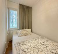 Hálószoba egy kétszobás lakásban ággyal, ablakkal és függönyökkel, fa dekorú padlóval.