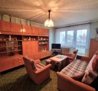 A háromszobás lakás nappalija retro bútorokkal és zöld szőnyeggel.