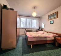 Hálószoba egy háromszobás lakásban, franciaággyal, szőnyeggel, bútorokkal és függönyökkel az ablakon.