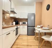 Konyha egy kétszobás lakásban fehér szekrényekkel és fa hatású padlóval.