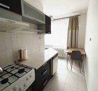 Konyha egy kétszobás lakásban tűzhellyel, sötét bútorokkal és világos csempével.