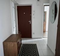 Folyosó egy kétszobás lakásban fehér csempével és fa berendezéssel.