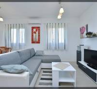 Nappali egy kétszobás lakásban kényelmes kanapéval, fehér bútorokkal és televízióval.