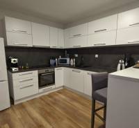 Konyha egy kétszobás lakásban fehér szekrényekkel és fa mintázatú padlóval.