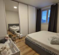 Hálószoba egy kétszobás lakásban fa mintázatú padlóval, ággyal és gyerekággyal.