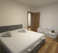 Hálószoba szürke ággyal és gyerekággyal, fa mintázatú padlóval egy kétszobás lakásban.