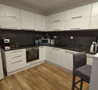 Két szobás lakás konyhája fa dekor padlóval és fehér szekrényekkel.