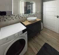 Fürdőszoba mosógéppel és mosdóval egy háromszobás lakásban, kis mozaik a falon.