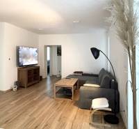 Nappali egy háromszobás lakásban, fa mintázatú padlóval és szürke kanapéval.